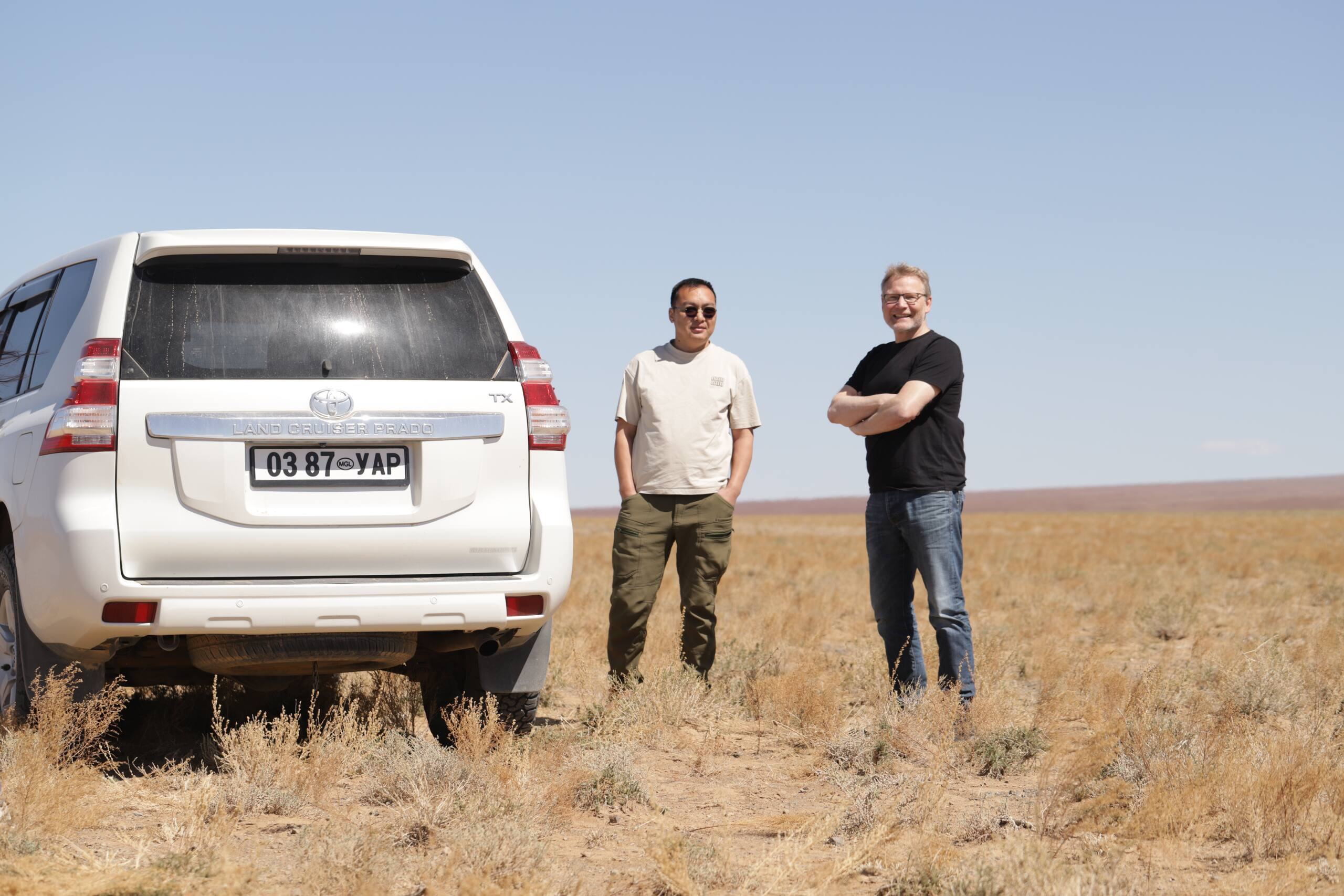 Tourists with tour guide standing next to white Land Cruiser in Gobi Desert