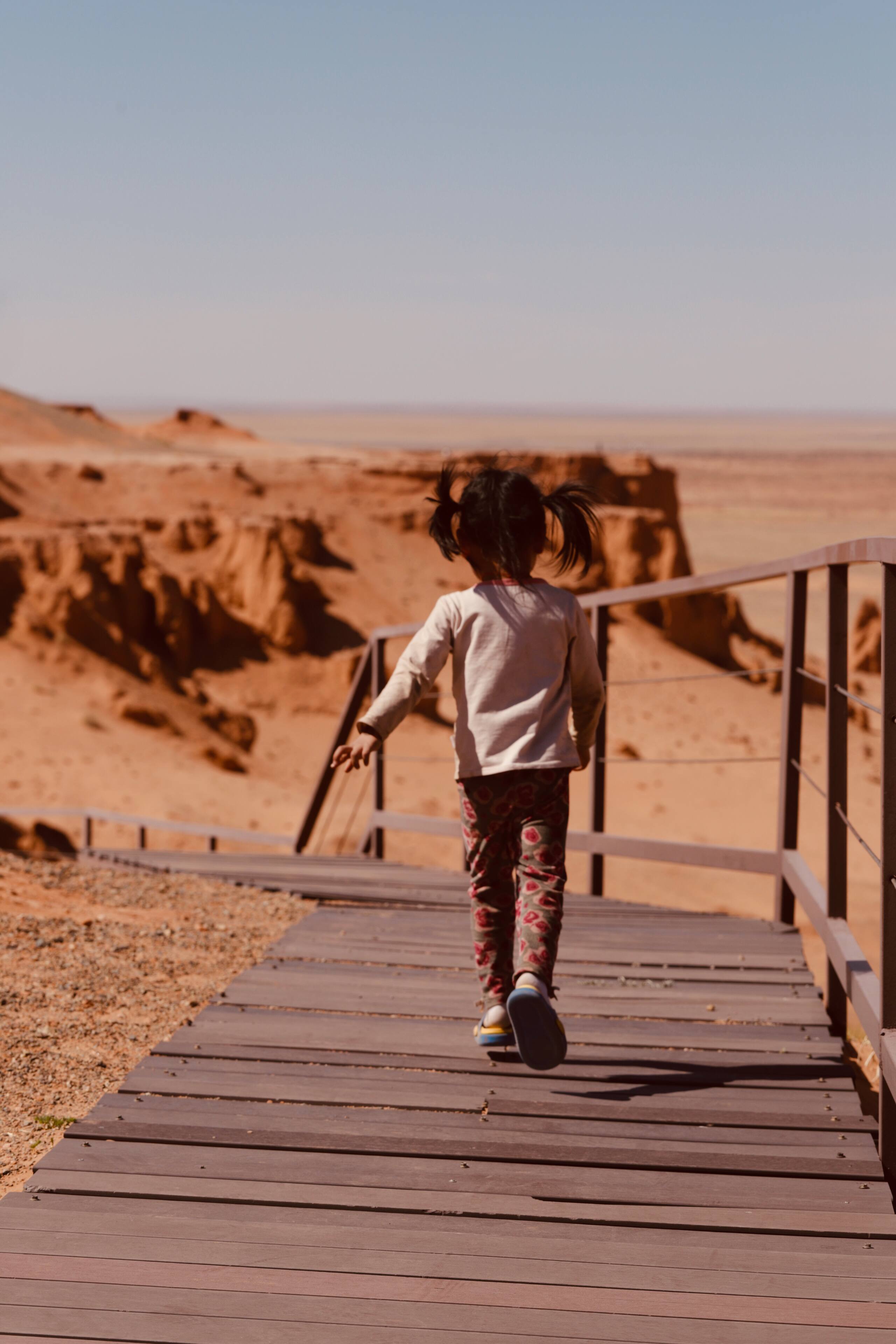Child running on wooden boardwalk at Bayanzag Flaming Cliffs